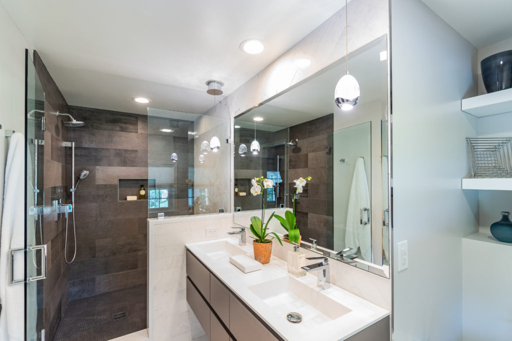 Homeowners wanted to create a sleek master bathroom, consistent with the design of their recently renovated home. To create the necessary square footage, the design combined the original master bathroom with a neighboring closet. This additional space became the new glass enclosed shower, with a custom quartz bench, glass hexagon grey mosaic floor tile, and Persian white marble herringbone accent wall. The new modern floating vanity provides ample storage as well as his and hers sinks.